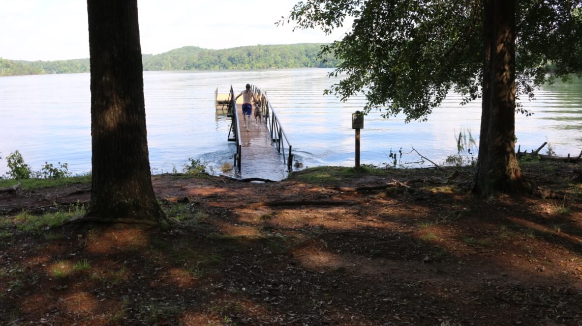 a boy and his dog running down the lake dock ramp and the entrance to the dock ramp is underwater